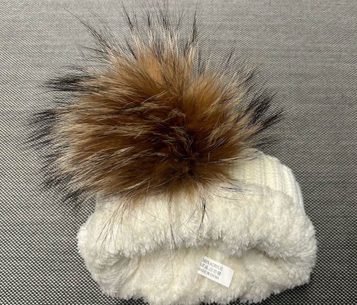 White knitted vest with large brown fur pompom, highlighting controversy over cat fur used despite wool labels White knitted vest with large brown fur pompom, highlighting controversy over cat fur used despite wool labels