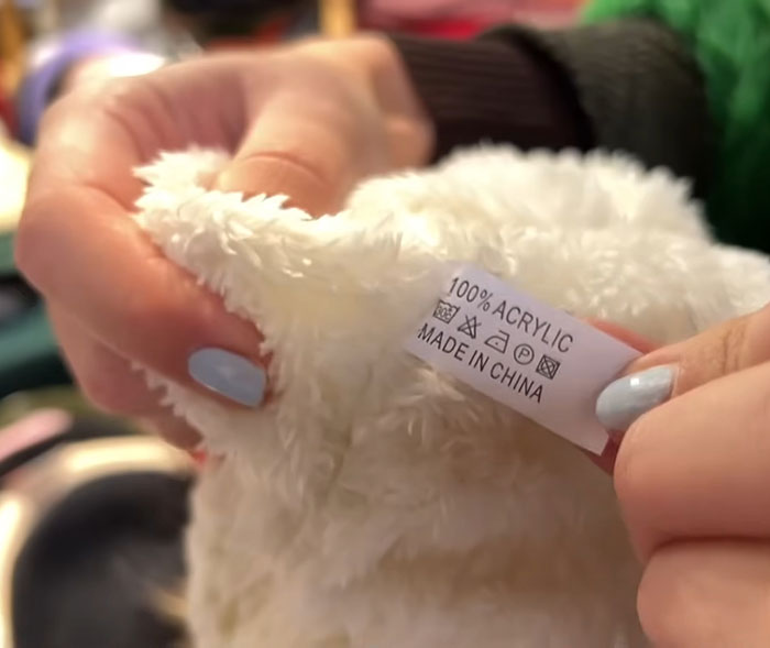 Hands holding a garment tag stating 100% acrylic fabric, linked to mass fury over cat fur used in fashion vests. Hands holding a garment tag stating 100% acrylic fabric, linked to mass fury over cat fur used in fashion vests.
