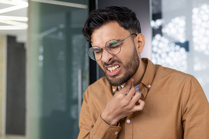 Man in glasses and brown shirt grimacing and scratching his neck, depicting reaction to coworker stealing spicy lunch. Man in glasses and brown shirt grimacing and scratching his neck, depicting reaction to coworker stealing spicy lunch.
