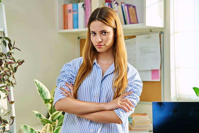 Young woman in a striped shirt with arms crossed, looking upset about coworker stealing her spicy lunch at the office. Young woman in a striped shirt with arms crossed, looking upset about coworker stealing her spicy lunch at the office.