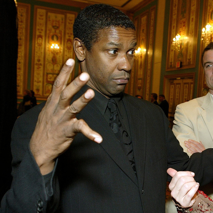 Man in black suit highlighting body abnormalities of his hand at an indoor event with ornate walls and decorations.