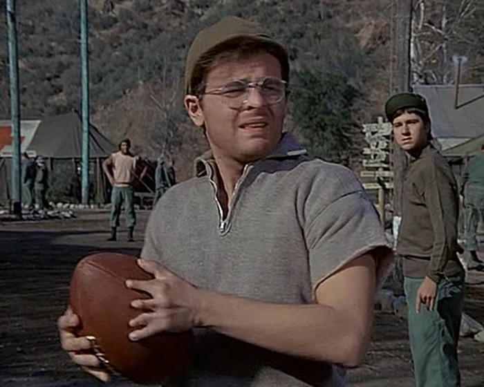 Actor in vintage military attire holding a football outdoors, illustrating celebrities with body abnormalities in a casual scene.