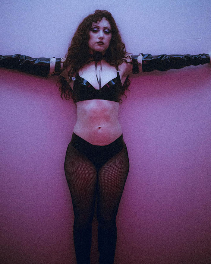 Chappell Roan posing confidently against a wall, showcasing her healthy body in black lingerie and gloves.