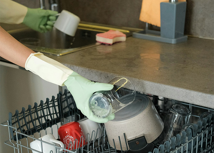 Person wearing gloves unloading clean dishes in dishwasher, illustrating habits that may improve your quality of life.