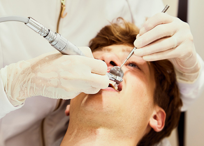 Dentist wearing gloves performing dental cleaning on a young man to improve his quality of life habits.