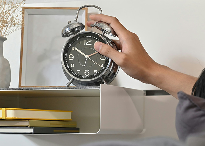 Hand reaching to turn off a vintage alarm clock on a nightstand, symbolizing habits to improve quality of life.