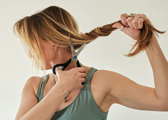 Woman with long hair cutting a braid with scissors, symbolizing habits that may improve your quality of life.