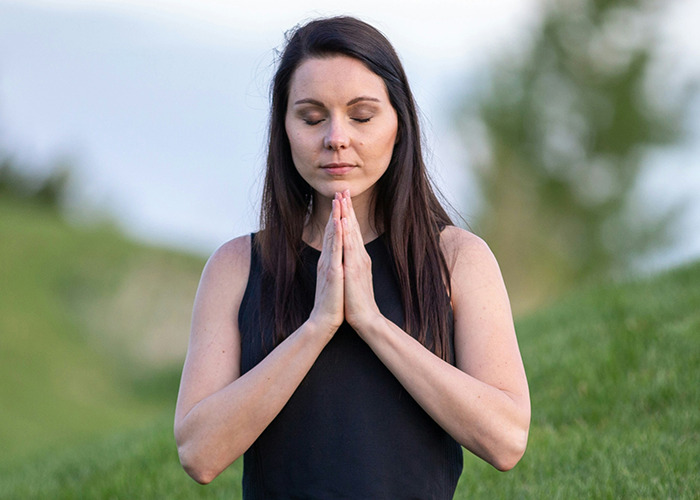 Woman meditating outdoors with eyes closed, practicing habits to improve quality of life in a peaceful natural setting.