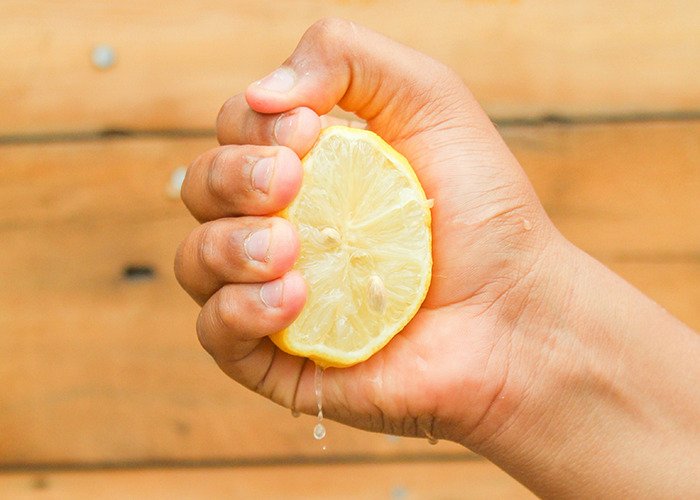 Hand squeezing lemon with juice dripping, illustrating healthy habits that may improve quality of life.