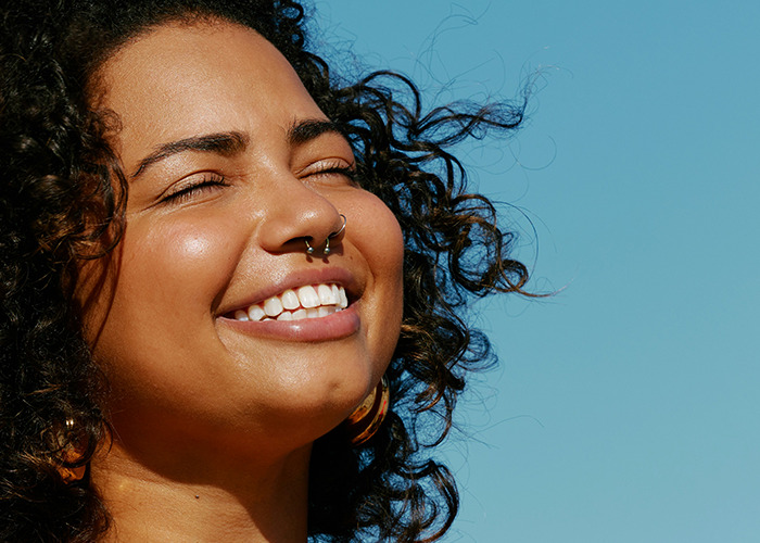 Smiling woman with curly hair enjoying sunlight outdoors, representing habits that improve quality of life and well-being.