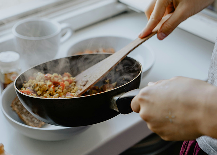 Hand cooking a healthy meal in a steaming frying pan demonstrating habits to improve quality of life according to netizens