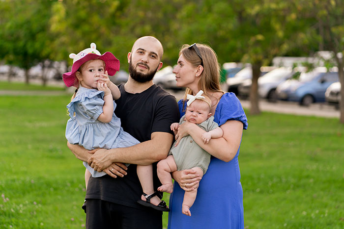 Family outdoors with a man hiding a secret second family, showing a wife and two young children in a park setting.