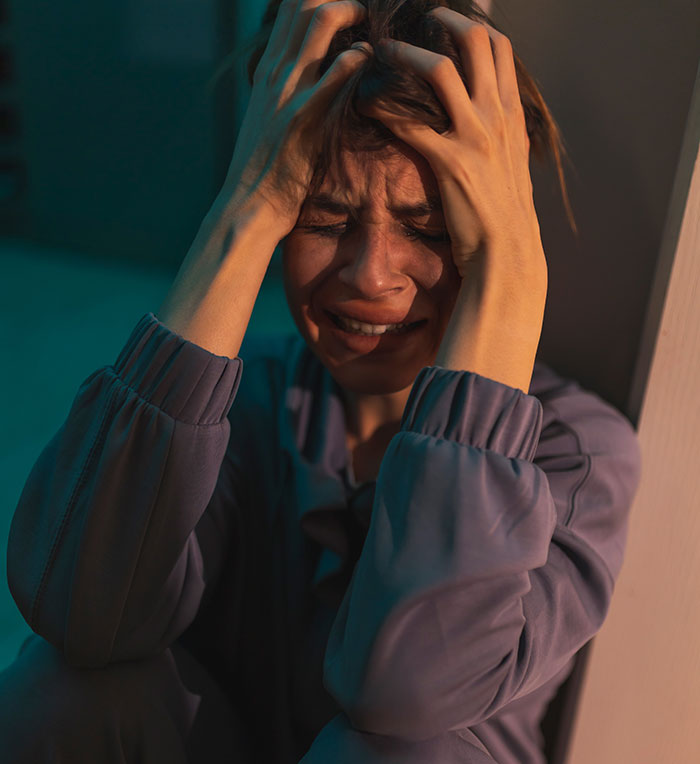 Woman sitting on the floor holding her head in distress after discovering her partner&rsquo;s secret second family.