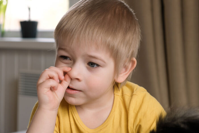 Young boy in a yellow shirt picking his nose indoors, illustrating common disgusting habits including nail biting and more.