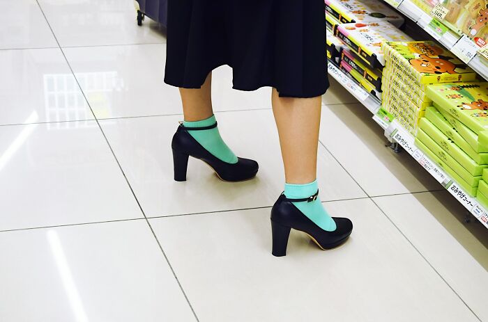 Person wearing black heels with turquoise socks standing on a tiled floor near store shelves in a shopping aisle.