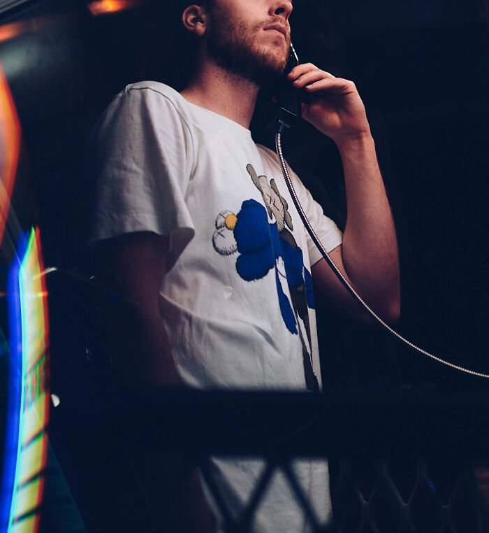 Young man speaking on a phone in a dim setting, reflecting on therapists and judgment moments in a casual environment.