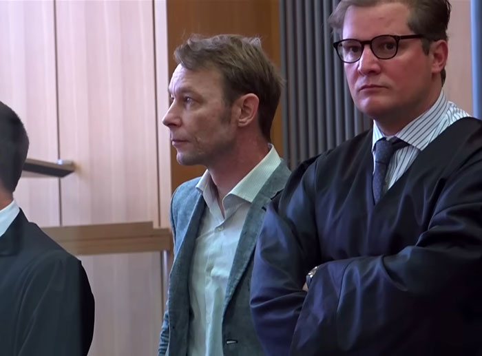 Two men, one in a suit and the other in legal robes, standing in a courtroom during the Madeleine McCann detectives investigation.