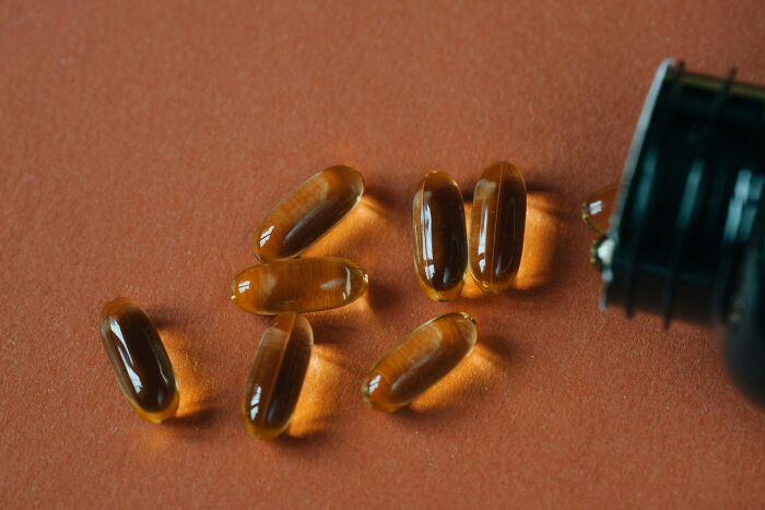 Softgel capsules spilled from a black bottle on an orange surface, one of the everyday items under $300.