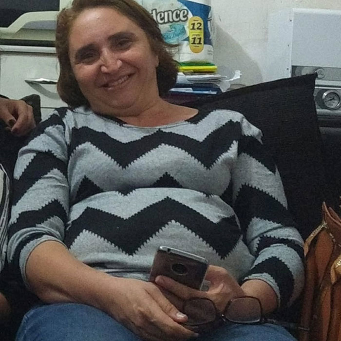Woman sitting and smiling, holding a phone, representing before-and-after photos of bodybuilding champion transformation.