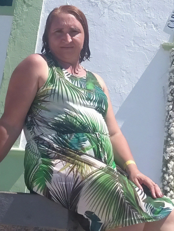Woman posing outdoors in a tropical dress before transformation into bodybuilding champion at age 53.