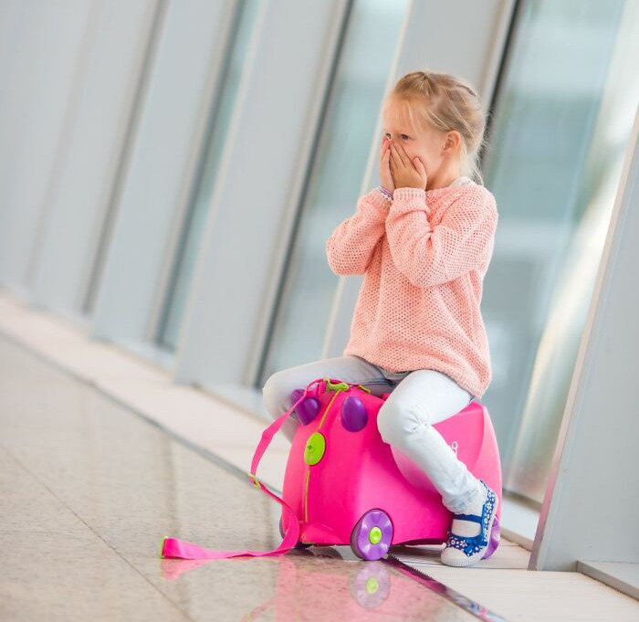 Little girl sitting on a pink suitcase at airport terminal showing unexpected airport security challenges.