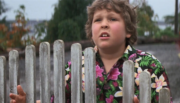 Child actor in a colorful floral shirt standing behind a wooden fence, symbolizing former Hollywood stars leaving the spotlight.