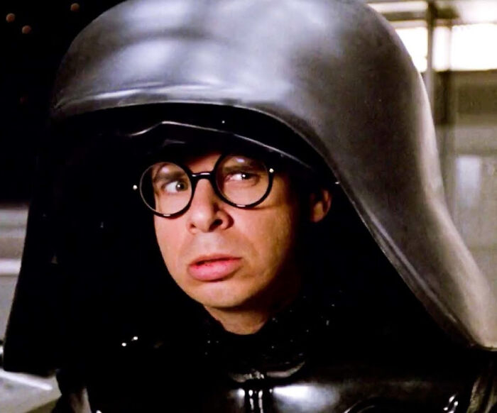 Actor in a black helmet and glasses portraying a comedic character from former Hollywood stars who left the spotlight.