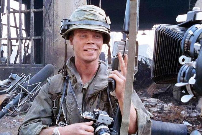 Former Hollywood star on a film set wearing military gear, holding a camera, highlighting career changes from the spotlight.