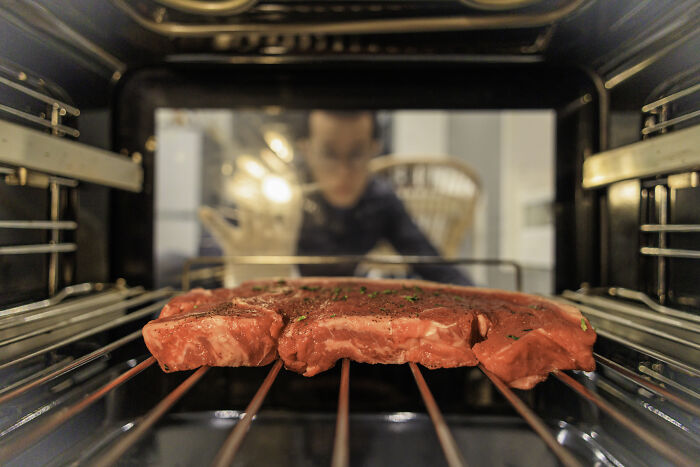 Raw steak inside an oven with a person blurred in the background, illustrating Americans reveal non-Americans food habits.