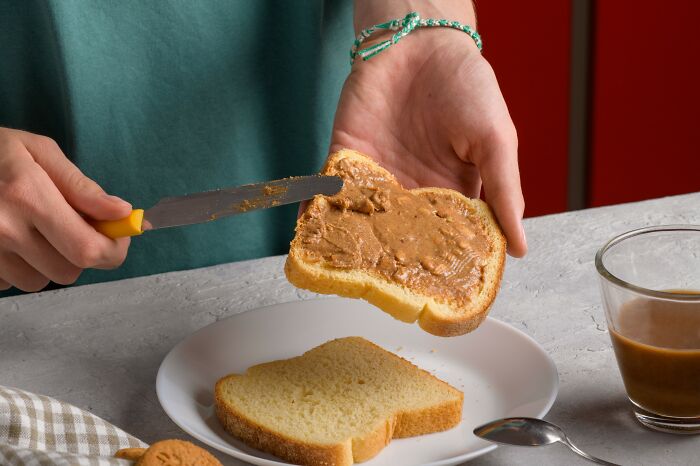 Person spreading peanut butter on bread, illustrating Americans reveal things non-Americans do like breaking spaghetti in front of Italians