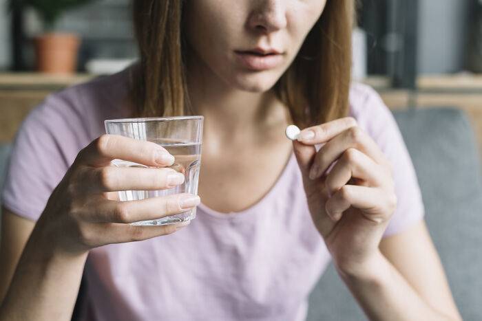 Woman holding a pill and glass of water, representing challenges faced with postpartum OCD symptoms and care.