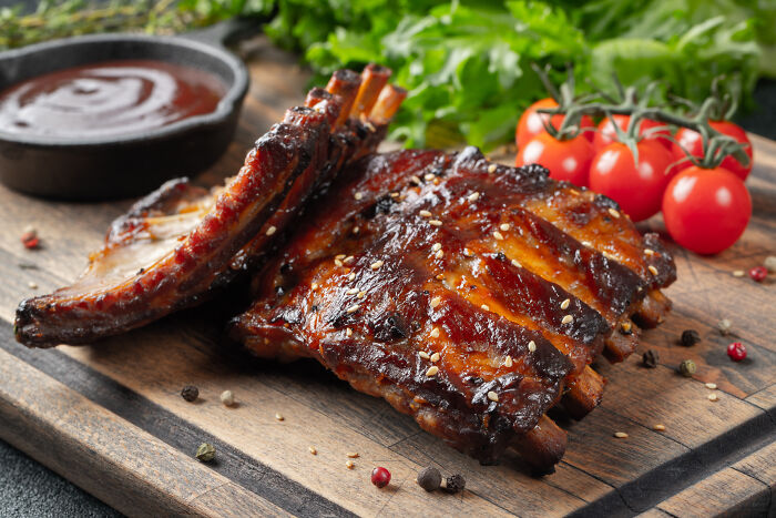 Barbecue ribs with sauce and tomatoes on wooden board, illustrating Americans reveal 30 things non-Americans do.
