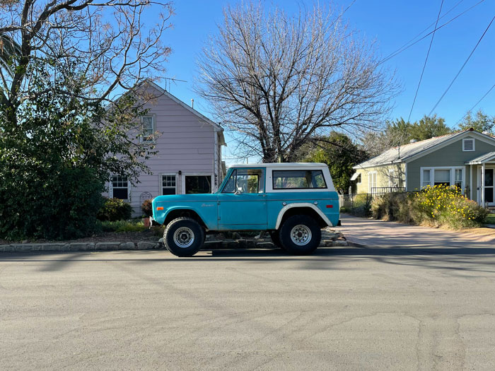 1972 Ford Bronco parked on a suburban street, surrounded by houses and leafless trees on a clear day