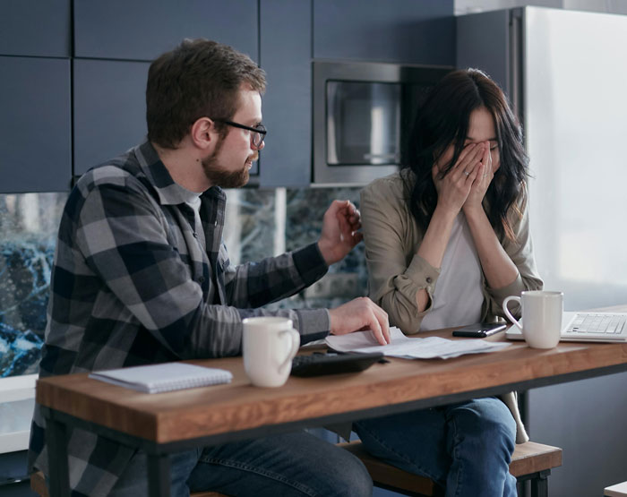 Man comforts distressed woman in kitchen, reflecting tension after buying 1972 Ford Bronco while wife is postpartum.