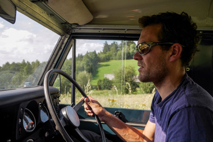 Man driving a vintage 1972 Ford Bronco in a countryside setting, chasing high school memories on a sunny day.