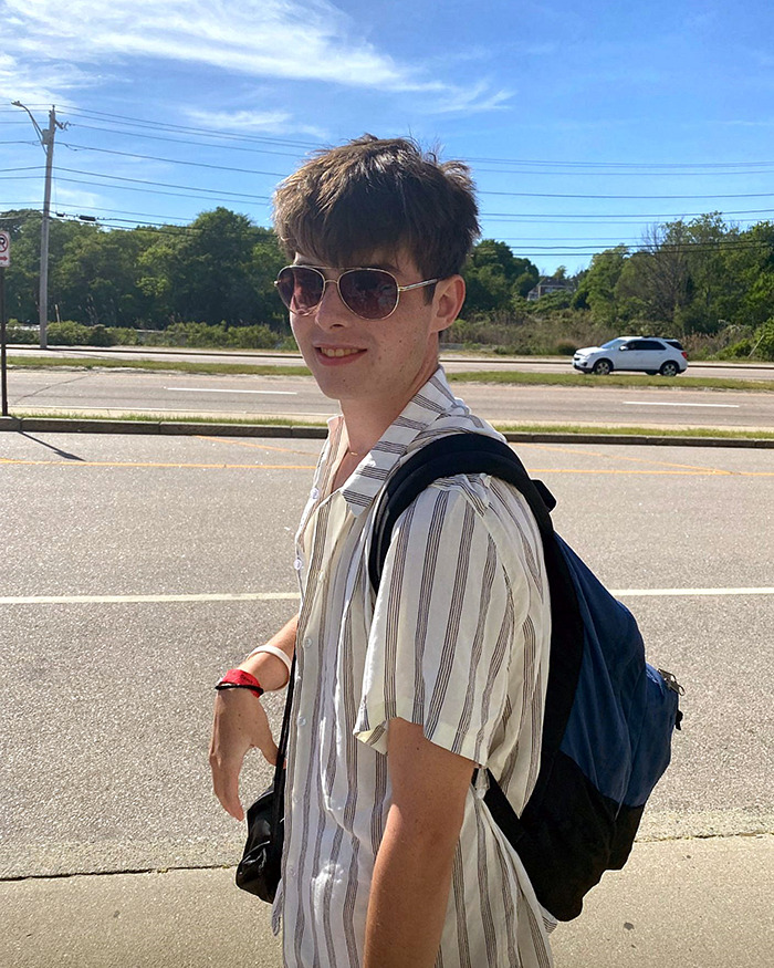 Young college student wearing sunglasses and a backpack standing outdoors near a road, days after graduating.