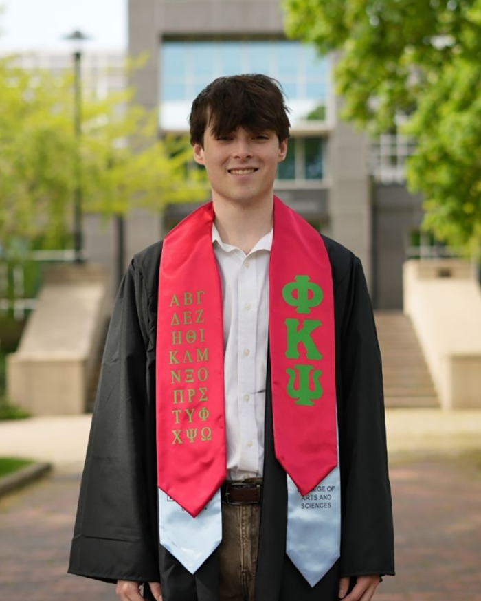 College student wearing graduation gown and stole, smiling outdoors after completing studies at university.