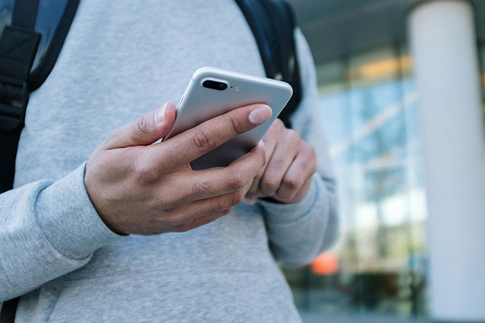 Person in gray sweatshirt holding smartphone outdoors illustrating woman at risk of not graduating failing to contribute to shared thesis