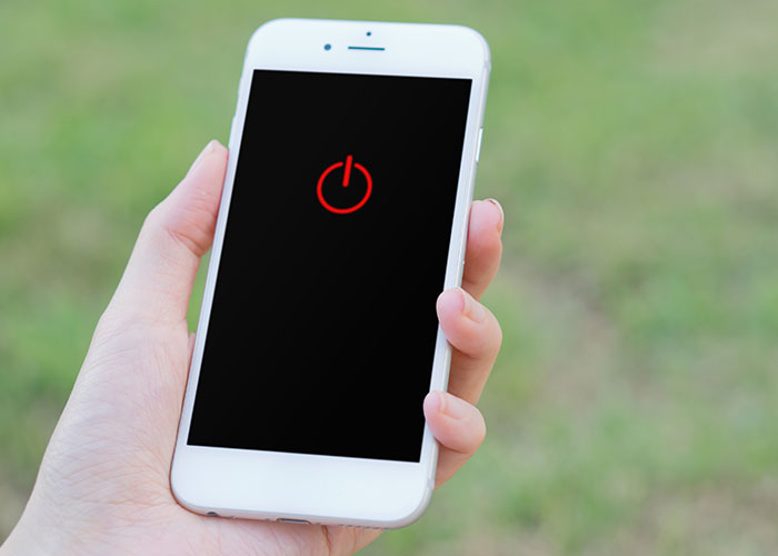 Hand holding white smartphone displaying red power symbol on black screen, representing employee compliance with company rules. Hand holding white smartphone displaying red power symbol on black screen, representing employee compliance with company rules.