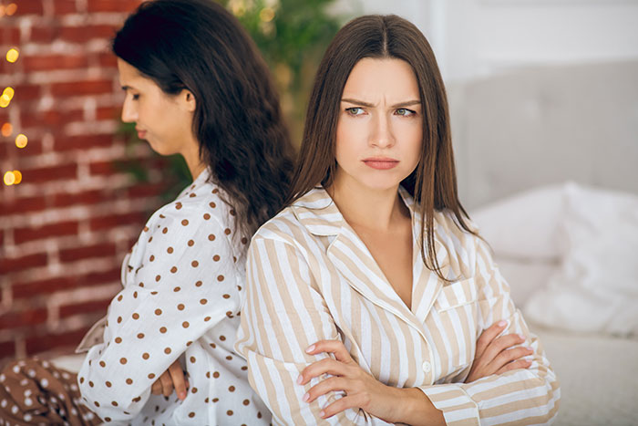 Two sisters in pajamas sitting back to back with crossed arms, showing tension in a wedding dress sisters drama.