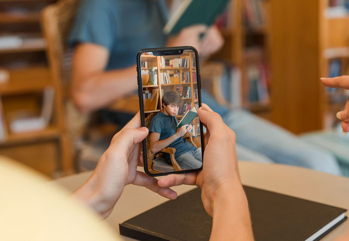 Person filming a guy speaking loudly in the library on a smartphone, capturing the disruptive behavior of the town jerk.