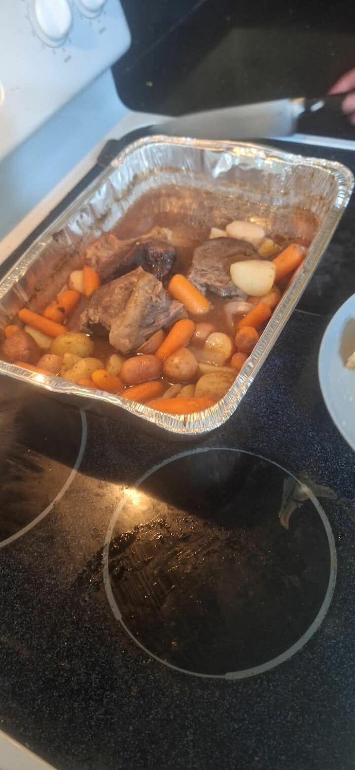 Aluminum tray with cooked meat, carrots, potatoes, and onions on a stovetop, an example of gross foods.