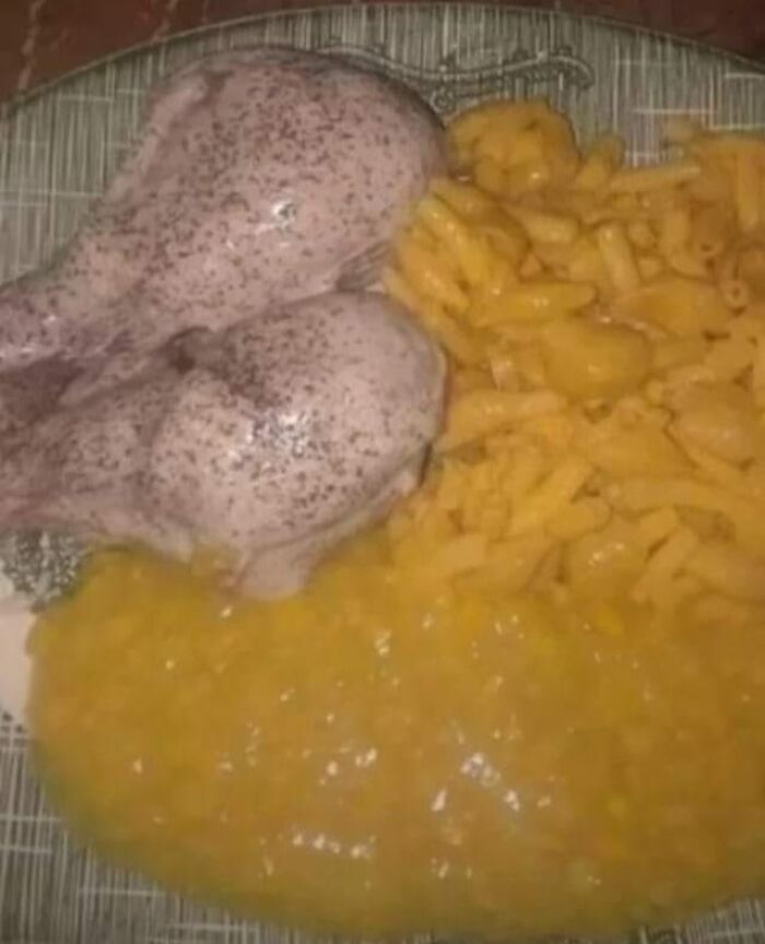 Plate with two uncooked raw chicken drumsticks, macaroni and cheese, and creamy corn, a gross food combination.
