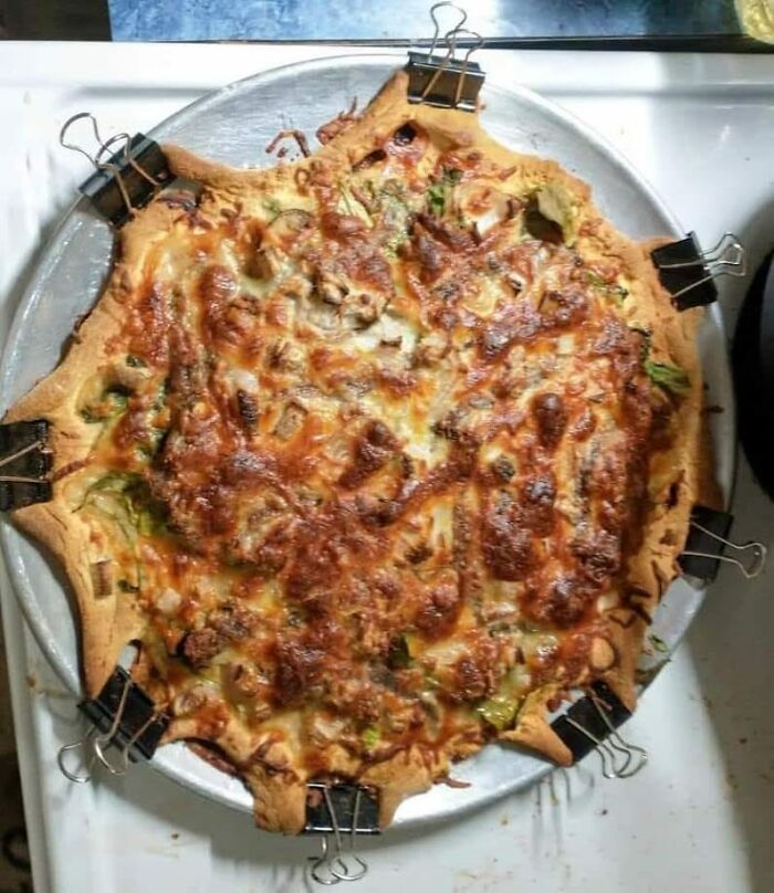 Unusually shaped homemade pizza with unevenly melted cheese, held in place by binder clips on a metal tray.