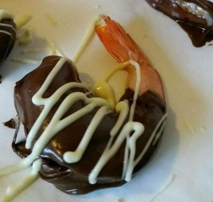 Shrimp covered in chocolate and white drizzle sauce on a white plate, an unusual gross food combination.