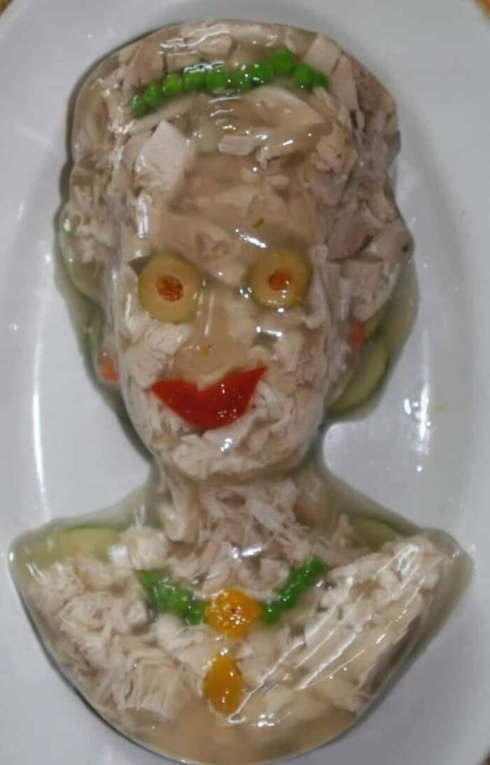 Jellied meat dish shaped like a face with olives for eyes and vegetables for decoration, a gross food example.
