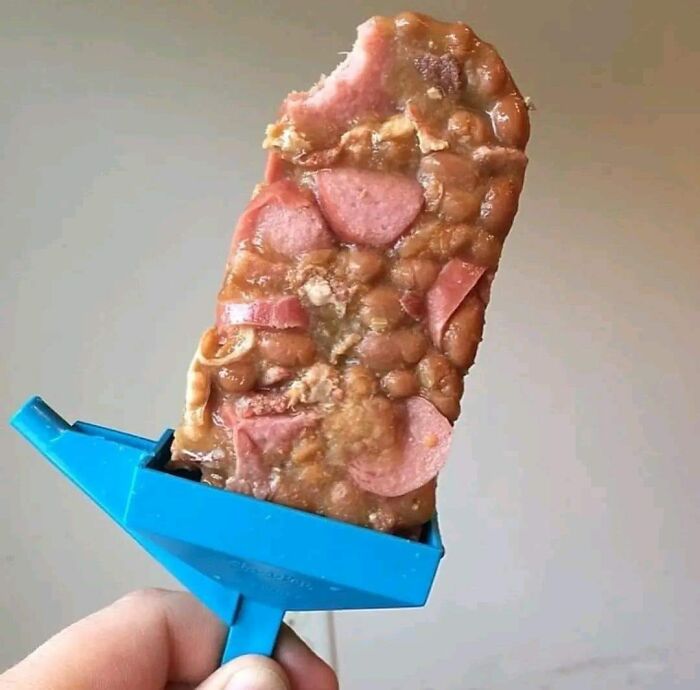 A hand holding a gross-looking food item with unappetizing textures and sliced meat pieces on a blue stick.