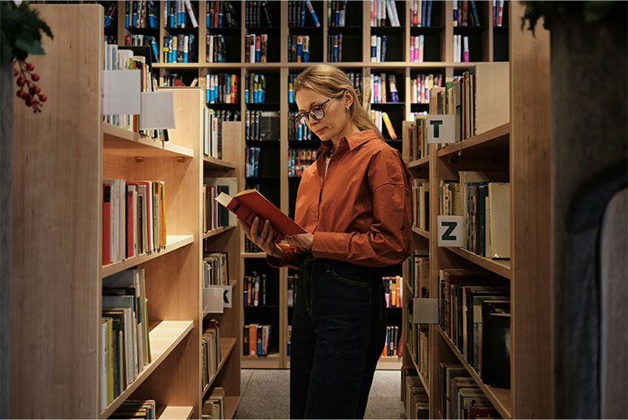 Young woman reading a book in a library, illustrating what the cool kids who peaked in high school are doing now.