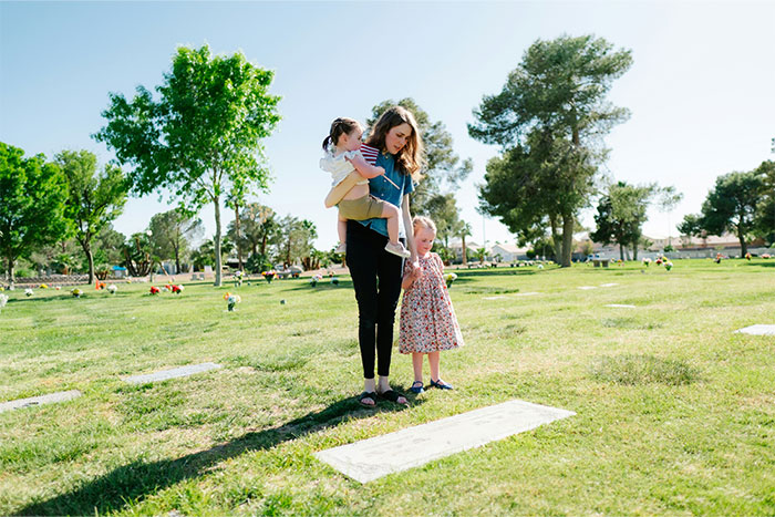 Woman holding a child and standing next to a girl in a park reflecting on life after the cool kids who peaked in high school.