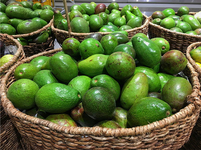 Basket baskets filled with green avocados stacked in a market, illustrating cool kids who peaked in high school today.